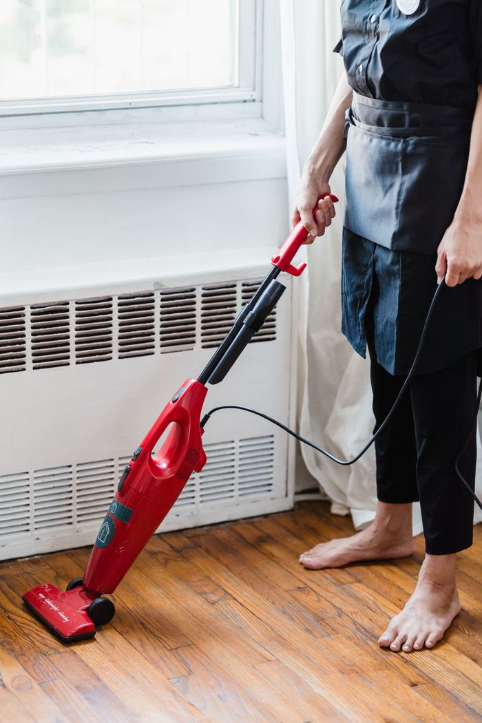 Personne nettoyant un sol en bois avec un aspirateur rouge dans une pièce bien éclairée.